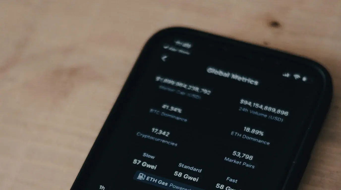 A phone resting on a light wooden surface, its dark screen listing market capitalisation, volume and gas-fee figures.