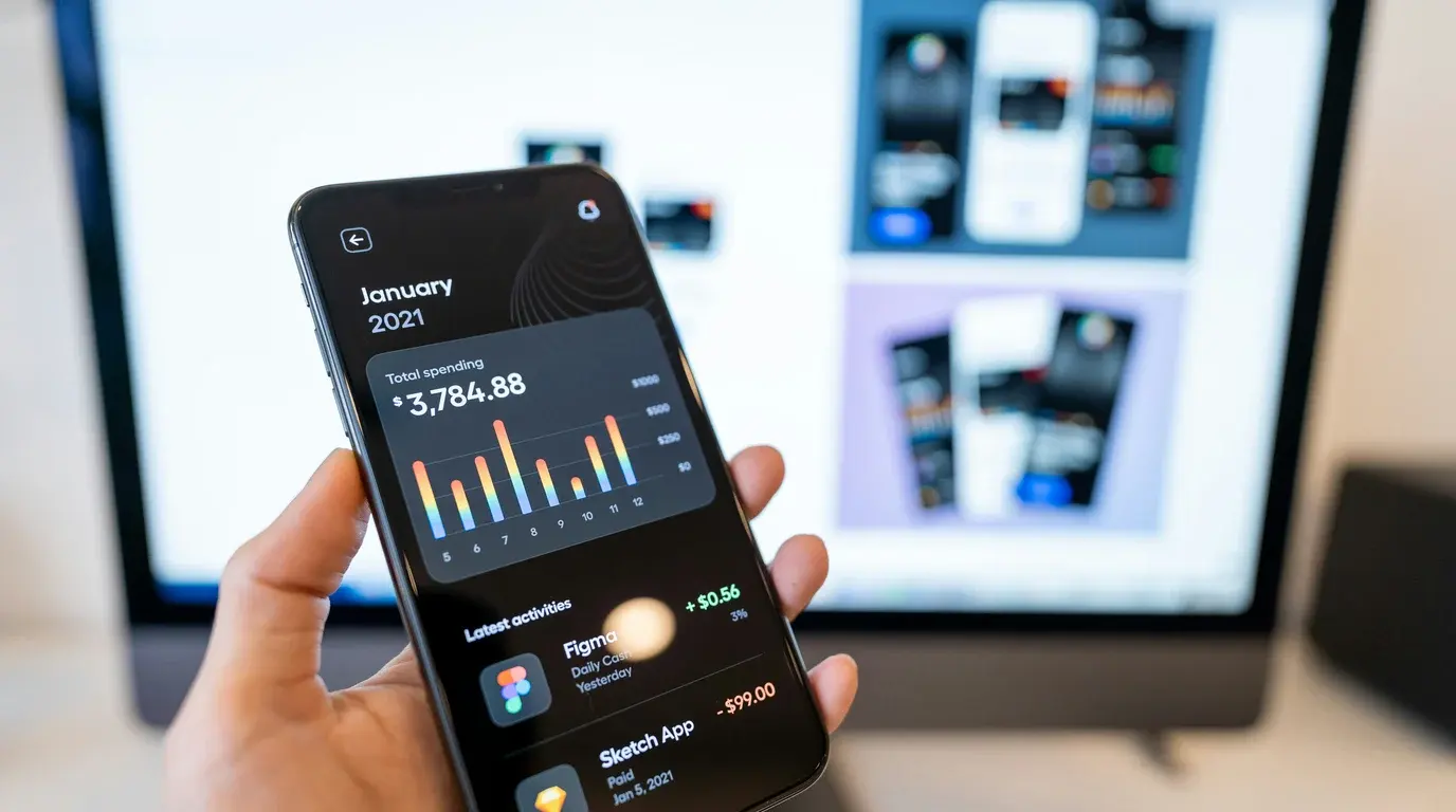 A hand holding a phone showing monthly spending totals, a colourful bar chart and a list of recent transactions.