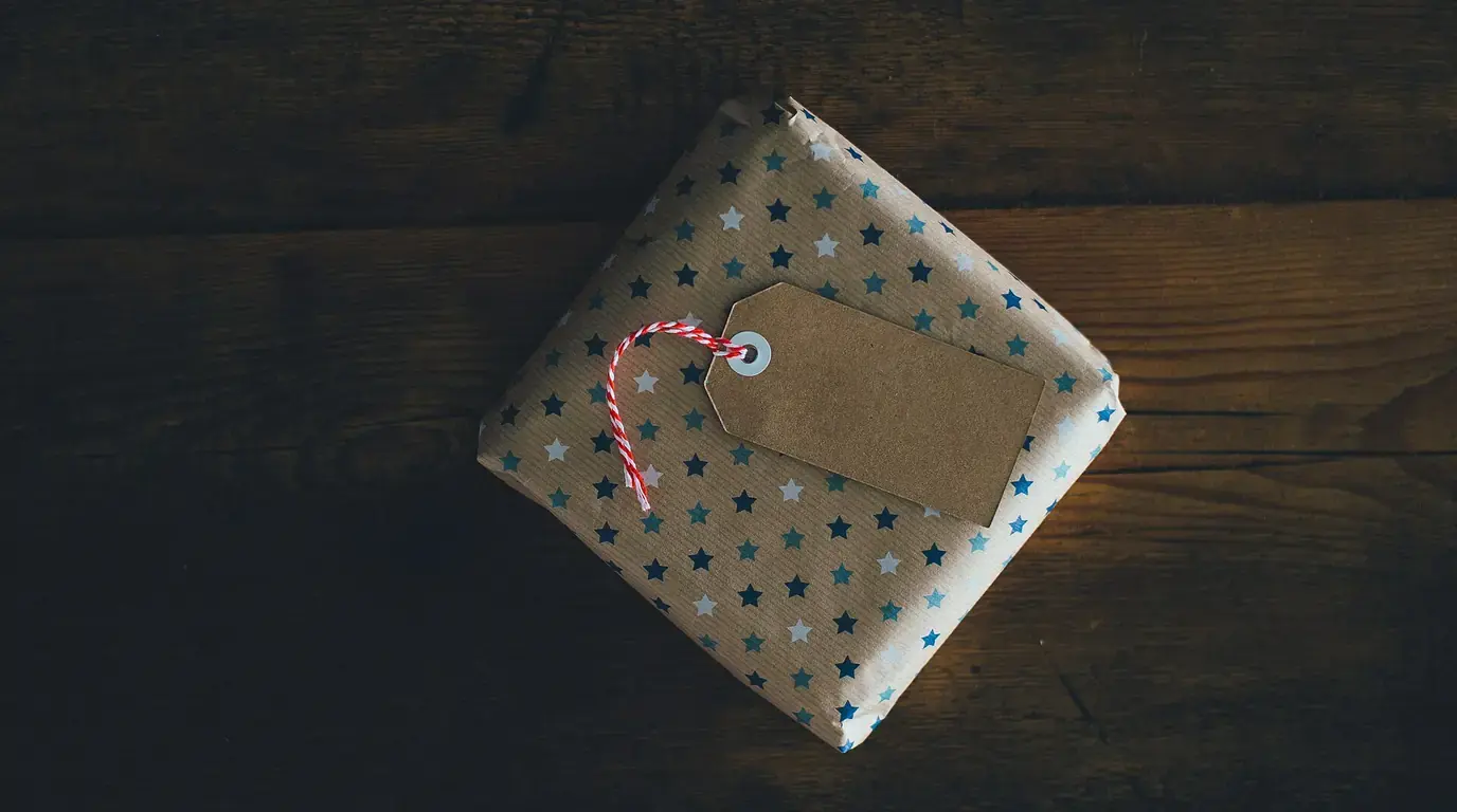 A small present wrapped in star-patterned paper with a blank brown gift tag and red-and-white string, on a dark wooden table.