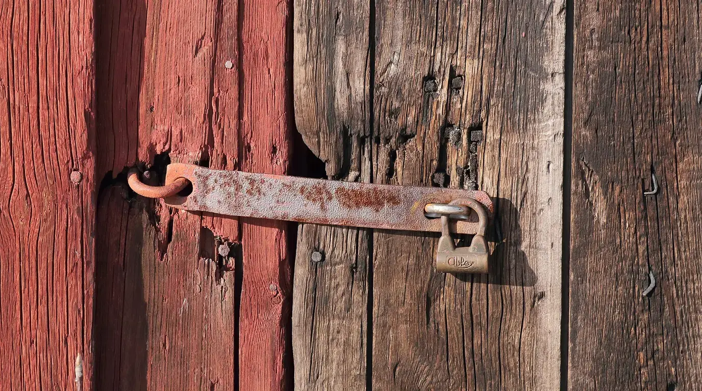 A rusty padlock fastening an iron hasp on an old red-painted wooden door.