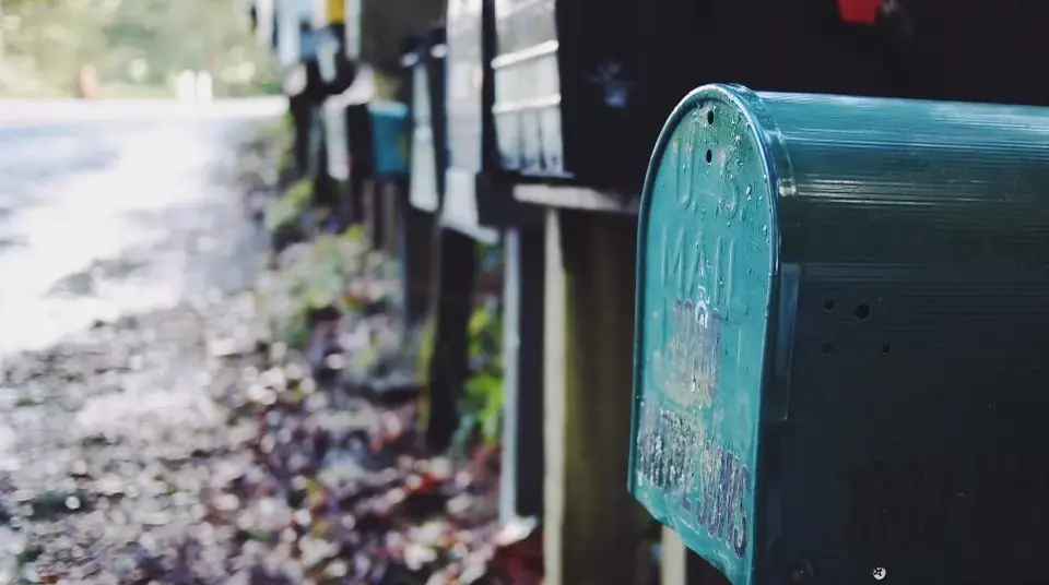 A row of old roadside mailboxes, a teal one in front, beside a leaf-strewn lane.