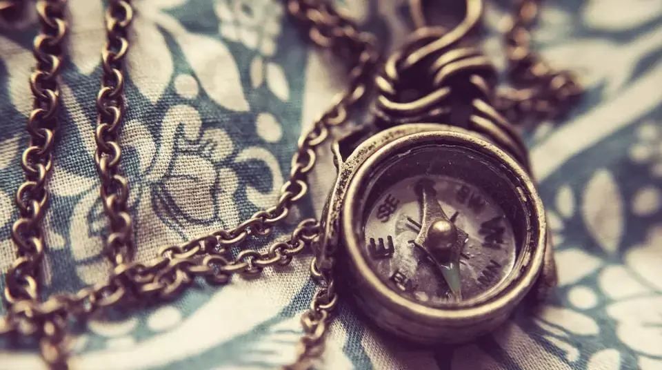 A small brass pocket compass on a chain, lying on patterned blue-and-cream fabric.